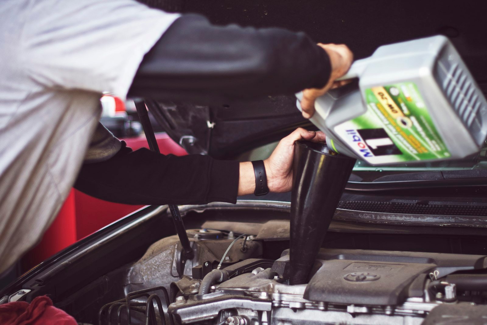 Person refilling motor oil into a car engine bay